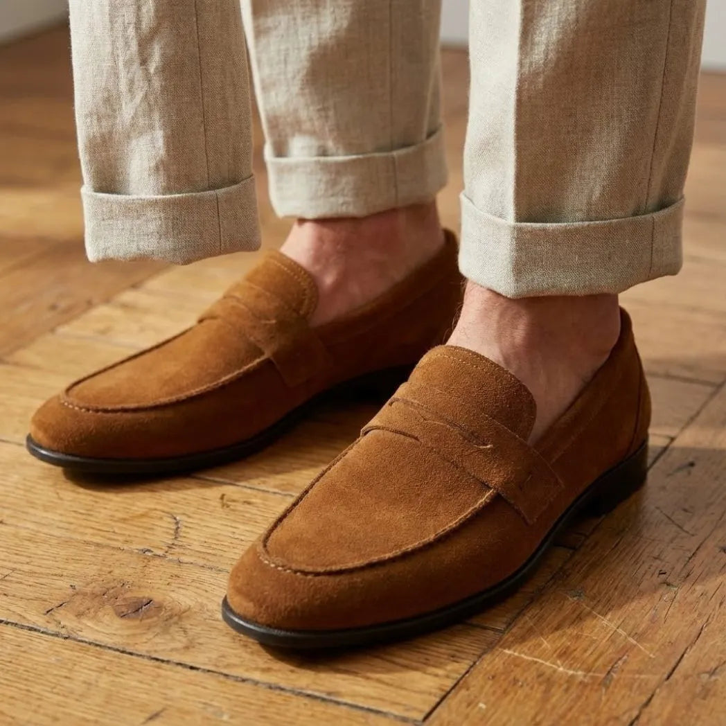 Mocassim Penny Loafer Milano Cognac: par marrom usado com calça clara dobrada na barra.