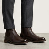 botas Chelsea Vitiello marrons usadas com calça cinza de barra dobrada.
