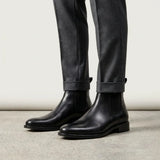 botas Chelsea Clássicas pretas usadas com calça cinza de barra dobrada.