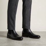 botas Chelsea Londres pretas usadas com calça cinza de barra dobrada.