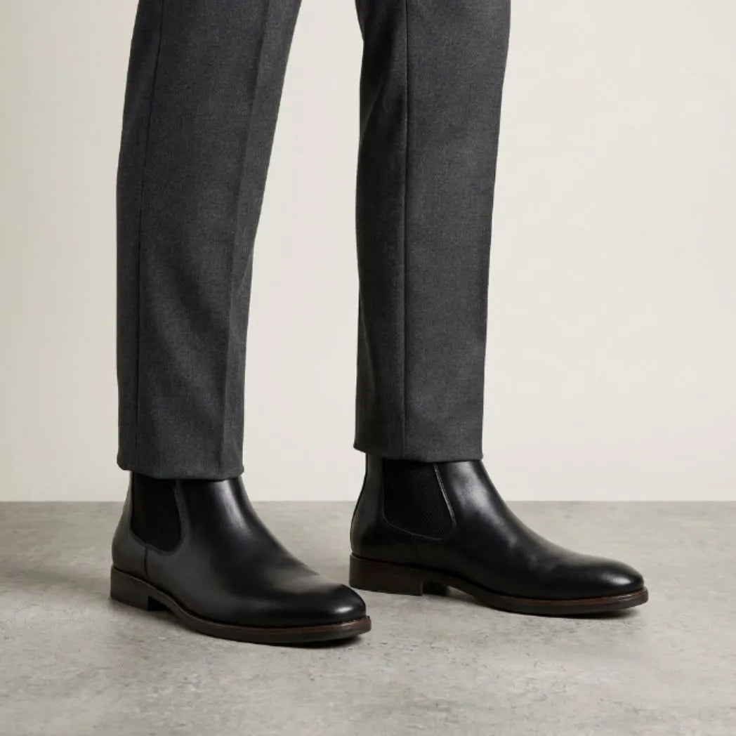 botas Chelsea Londres pretas usadas com calça cinza de barra dobrada.