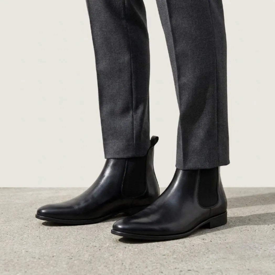 botas Chelsea Nobre pretas usadas com calça cinza de barra dobrada.