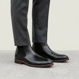 botas Chelsea Milan pretas usadas com calça cinza de barra dobrada.