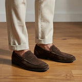 Mocassim Penny Loafer Milano Cognac: par marrom-escuro usado com calça clara dobrada na barra.