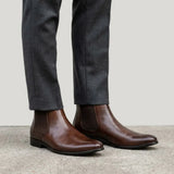 botas Chelsea Nobre marrons usadas com calça cinza de barra dobrada.