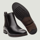 Par de botas Chelsea Londres pretas, com um dos solados voltado para a câmera.