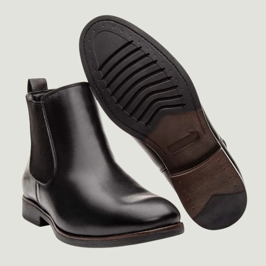 Par de botas Chelsea Londres pretas, com um dos solados voltado para a câmera.