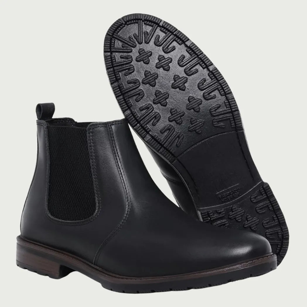 Par de botas Chelsea Sítio pretas, com um dos solados voltado para a câmera.