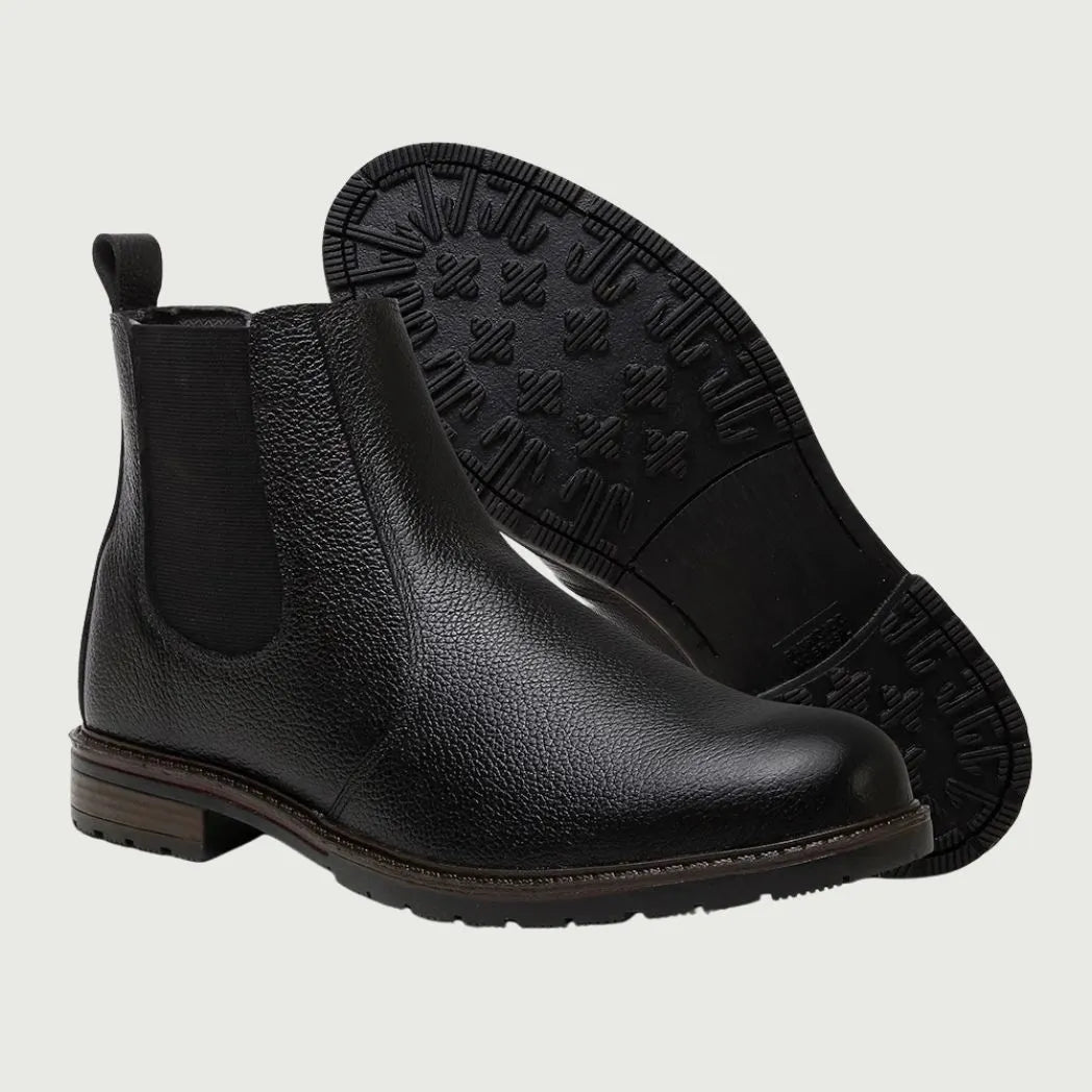 Par de botas Chelsea Vitiello pretas, com um dos solados voltado para a câmera.