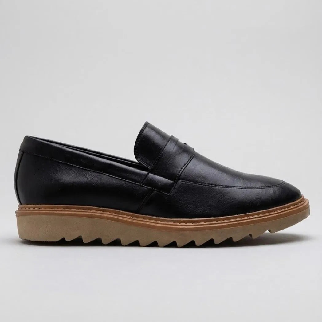 Mocassim Ash Tratorado: modelo preto de perfil, com faixa frontal, borda marrom e sola bege com sulcos profundos.