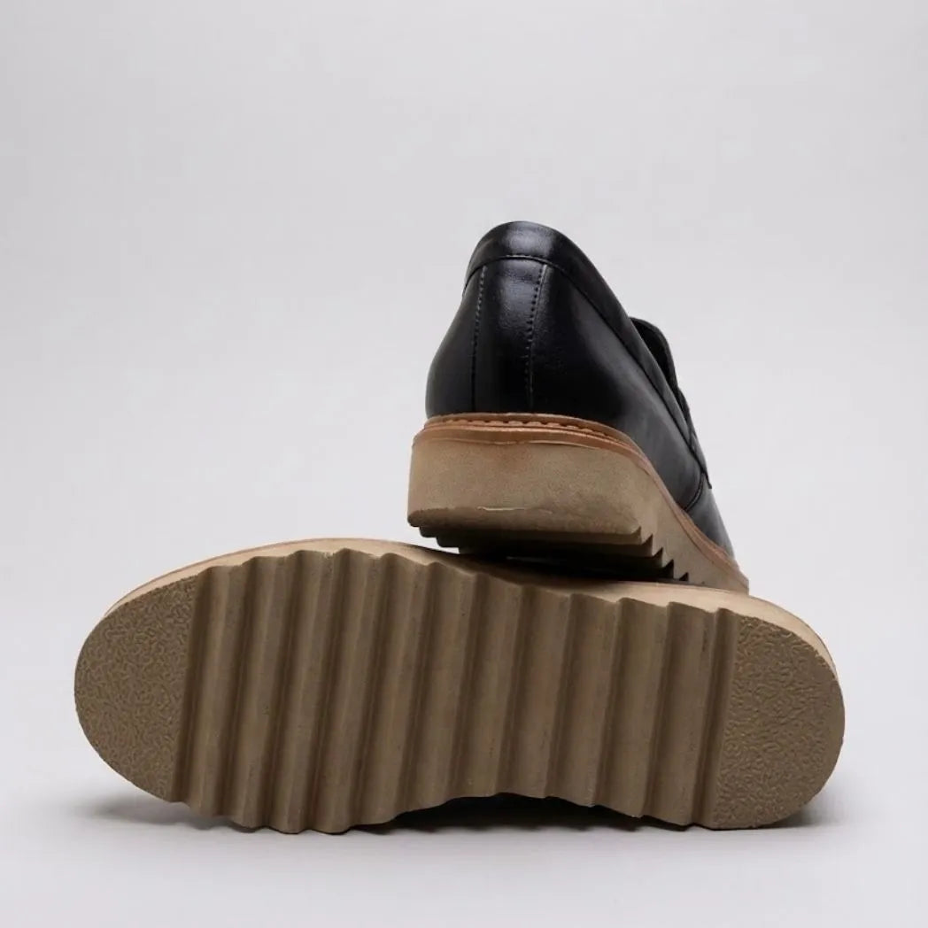 Par do modelo Mocassim Ash Tratorado, na cor preto, com um dos solados voltado para a câmera.