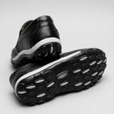 Mocassim Casual Comfort Daytona Drive: par preto com um sapato virado, mostrando a sola preta com detalhes ovais claros.