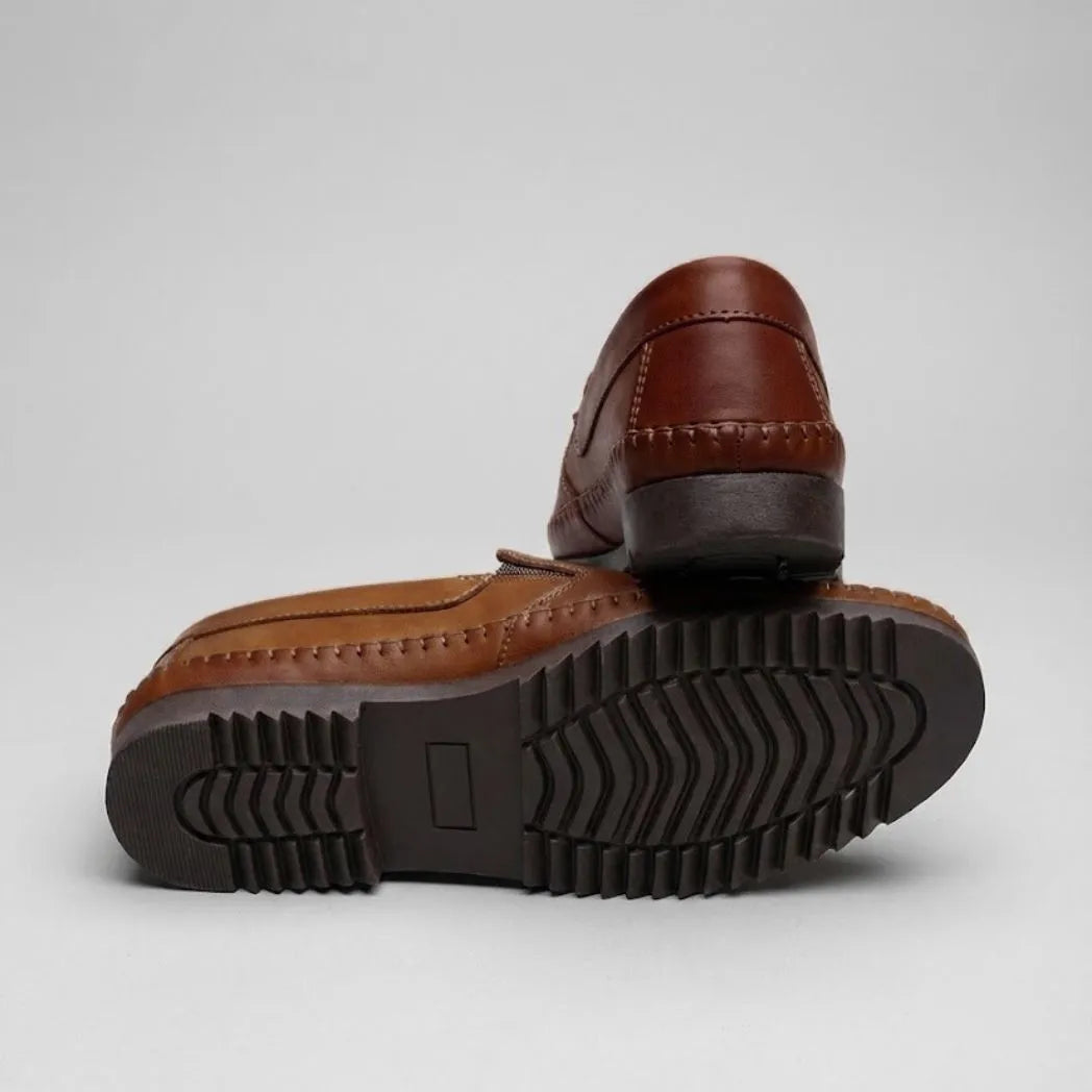 Mocassim Casual Dakota Rust: par marrom com um sapato virado, mostrando a sola preta com sulcos.