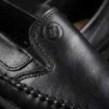 Mocassim Casual Dakota Rust: detalhe da superfície preta, do emblema circular em relevo e da costura.