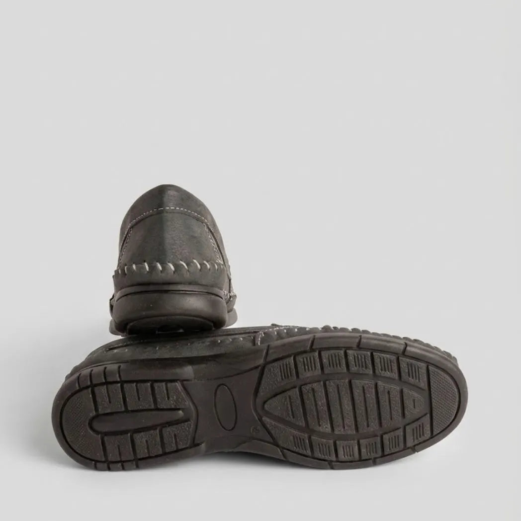 Par do modelo Mocassim Cognac de Couro, na cor cinza-escuro, com um dos solados voltado para a câmera.