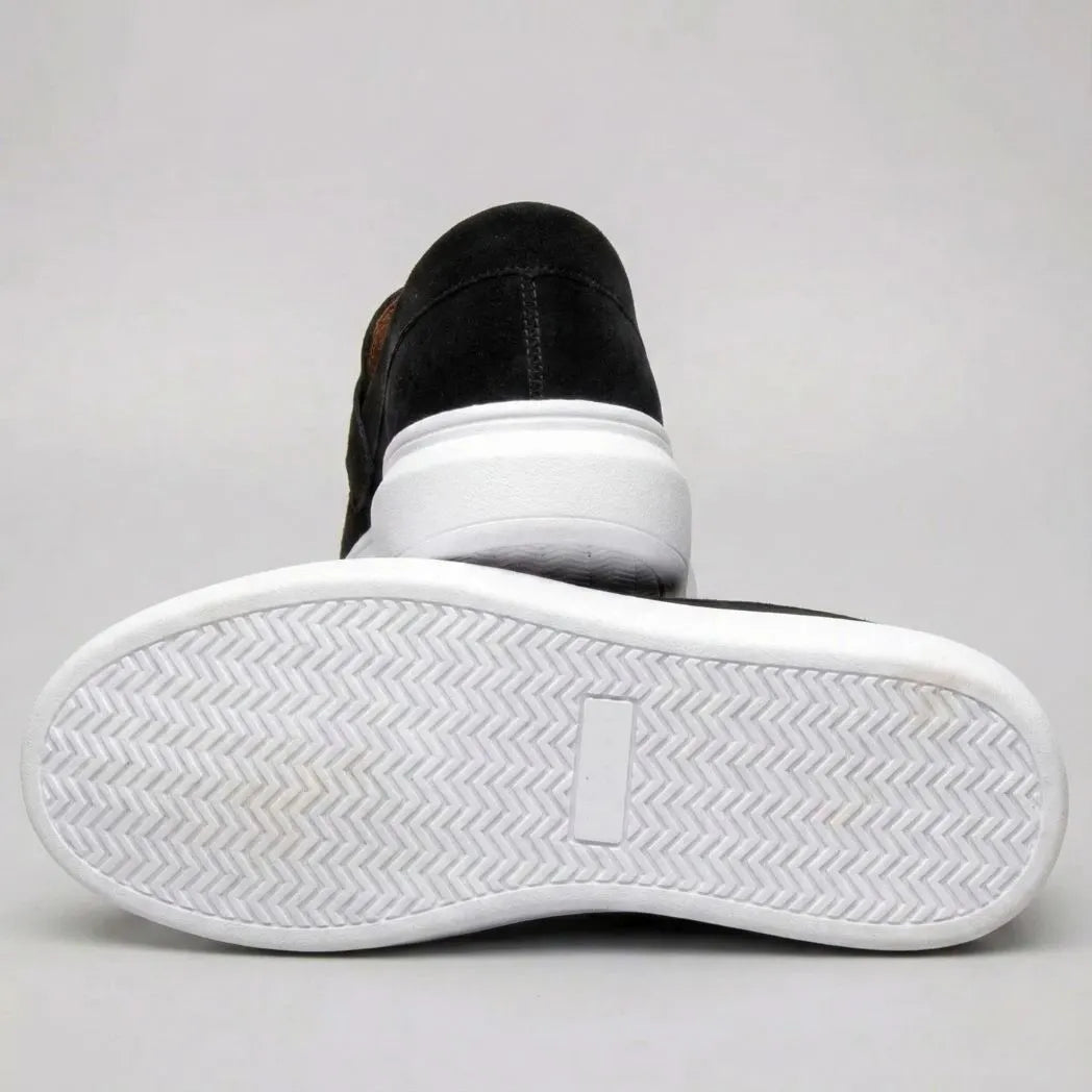 Mocassim Derby de Camurça: par preto com um sapato virado, mostrando a sola branca com relevo em zigue-zague.