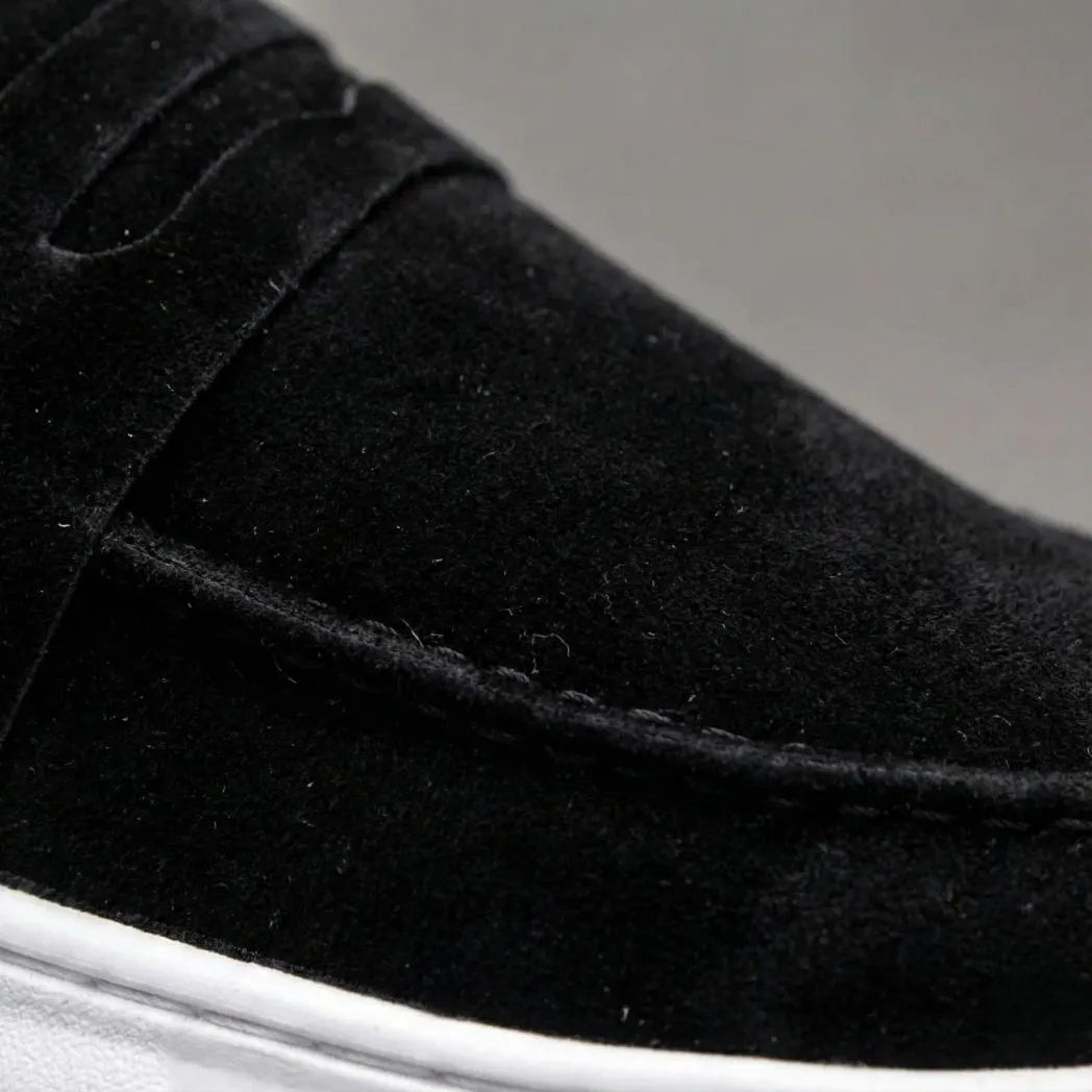 Mocassim Derby de Camurça: detalhe da textura preta, da faixa frontal e da costura.