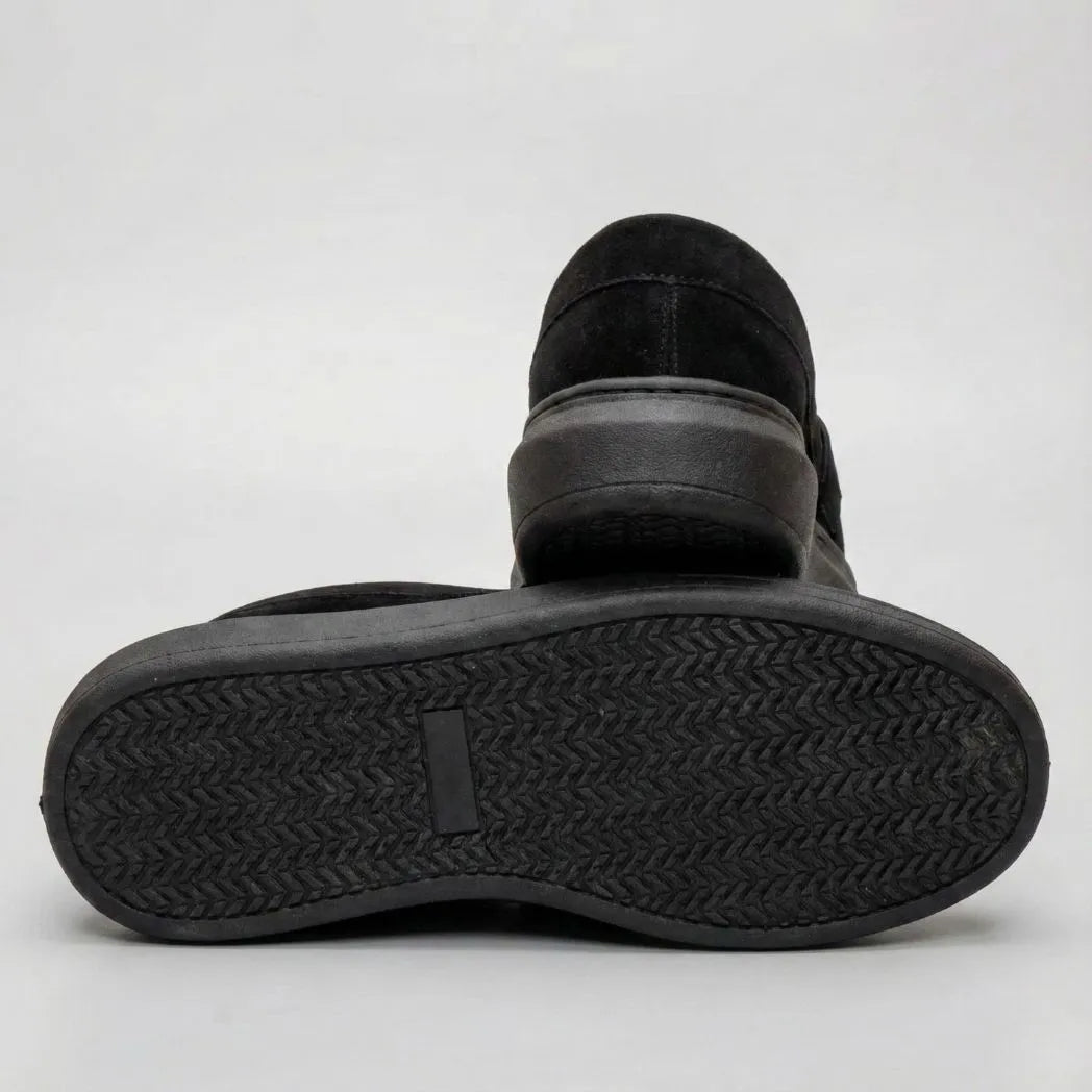 Mocassim Derby de Camurça: par preto com um sapato virado, mostrando a sola preta com relevo em zigue-zague.