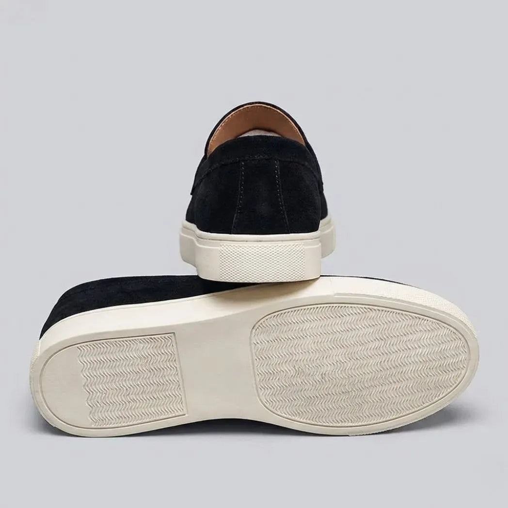 Par do modelo Mocassim Derby de Camurça com Guizos, na cor preto, com um dos solados voltado para a câmera.