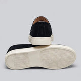 Par do modelo Mocassim Derby de Camurça com Guizos, na cor preto, com um dos solados voltado para a câmera.
