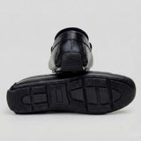 Par do modelo Mocassim Driver Aero Bit com Fivela, na cor preto, com um dos solados voltado para a câmera.
