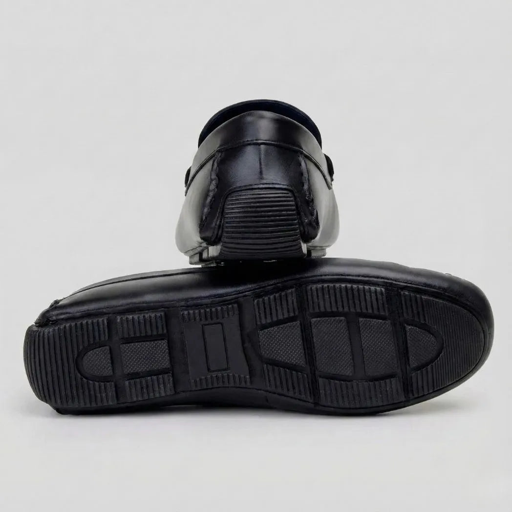 Par do modelo Mocassim Driver Aero Bit com Fivela, na cor preto, com um dos solados voltado para a câmera.