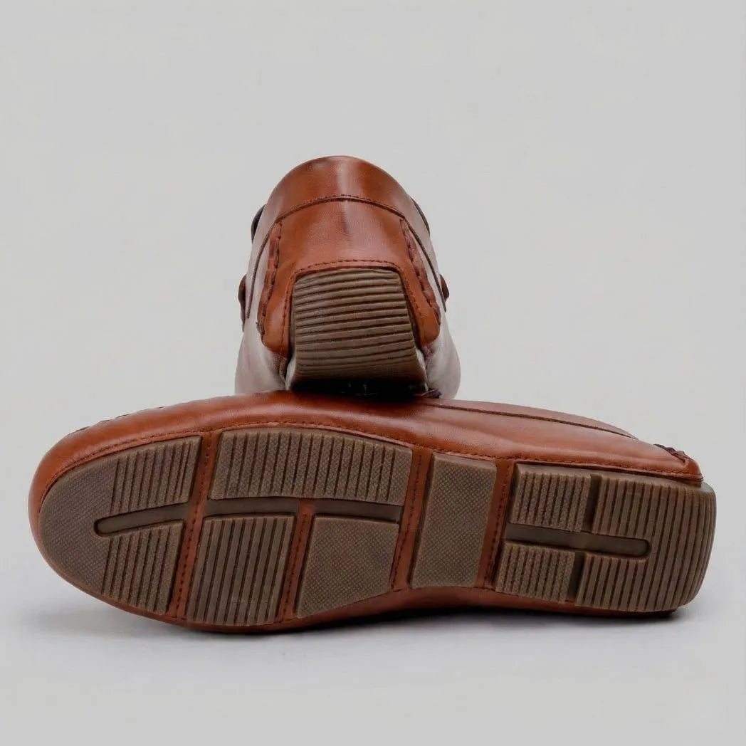 Par do modelo Mocassim Driver Aero Bit com Fivela, na cor marrom, com um dos solados voltado para a câmera.
