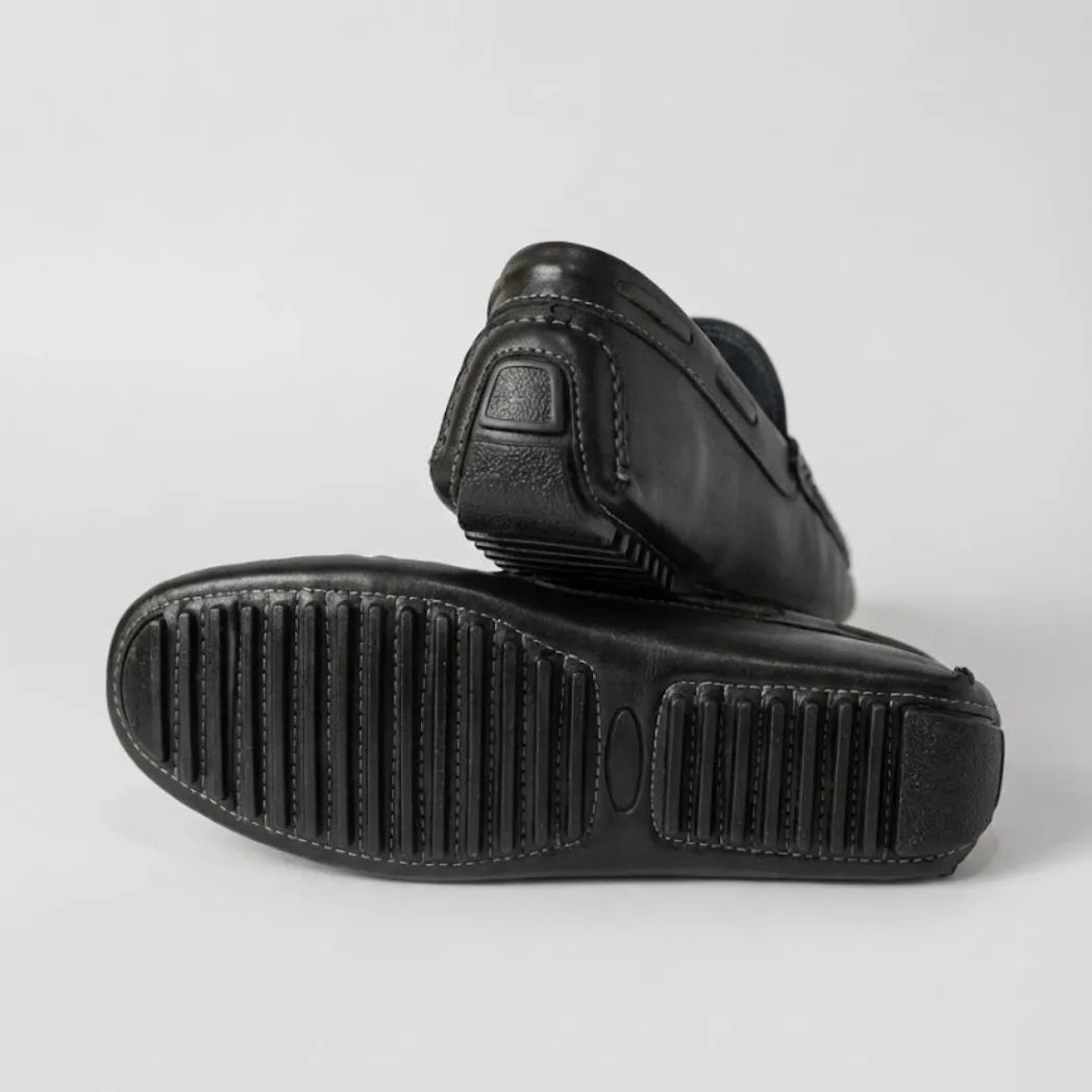 Par do modelo Mocassim Driver Cruise de Couro Preto, na cor preto, com um dos solados voltado para a câmera.