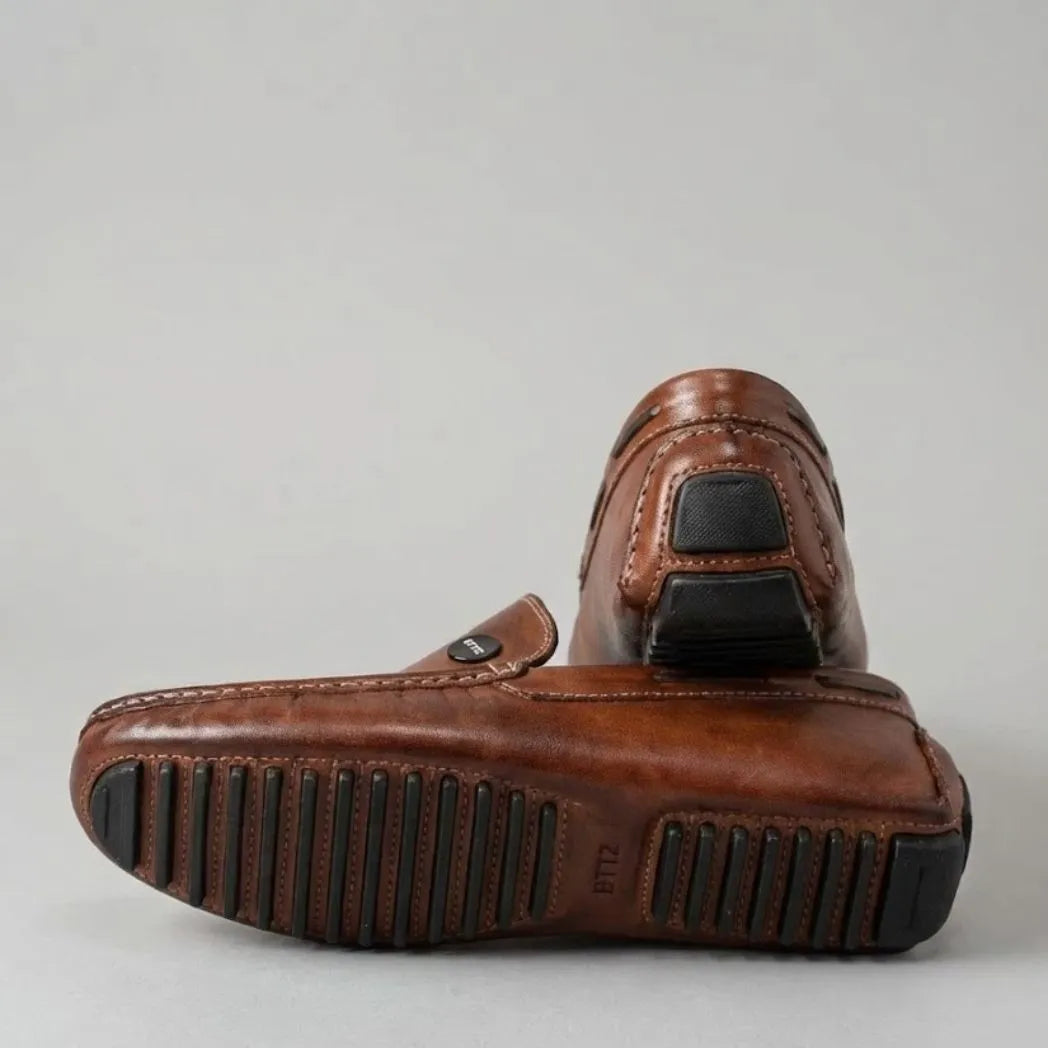 Par do modelo Mocassim Driver Cruise de Couro Marrom, na cor marrom, com um dos solados voltado para a câmera.