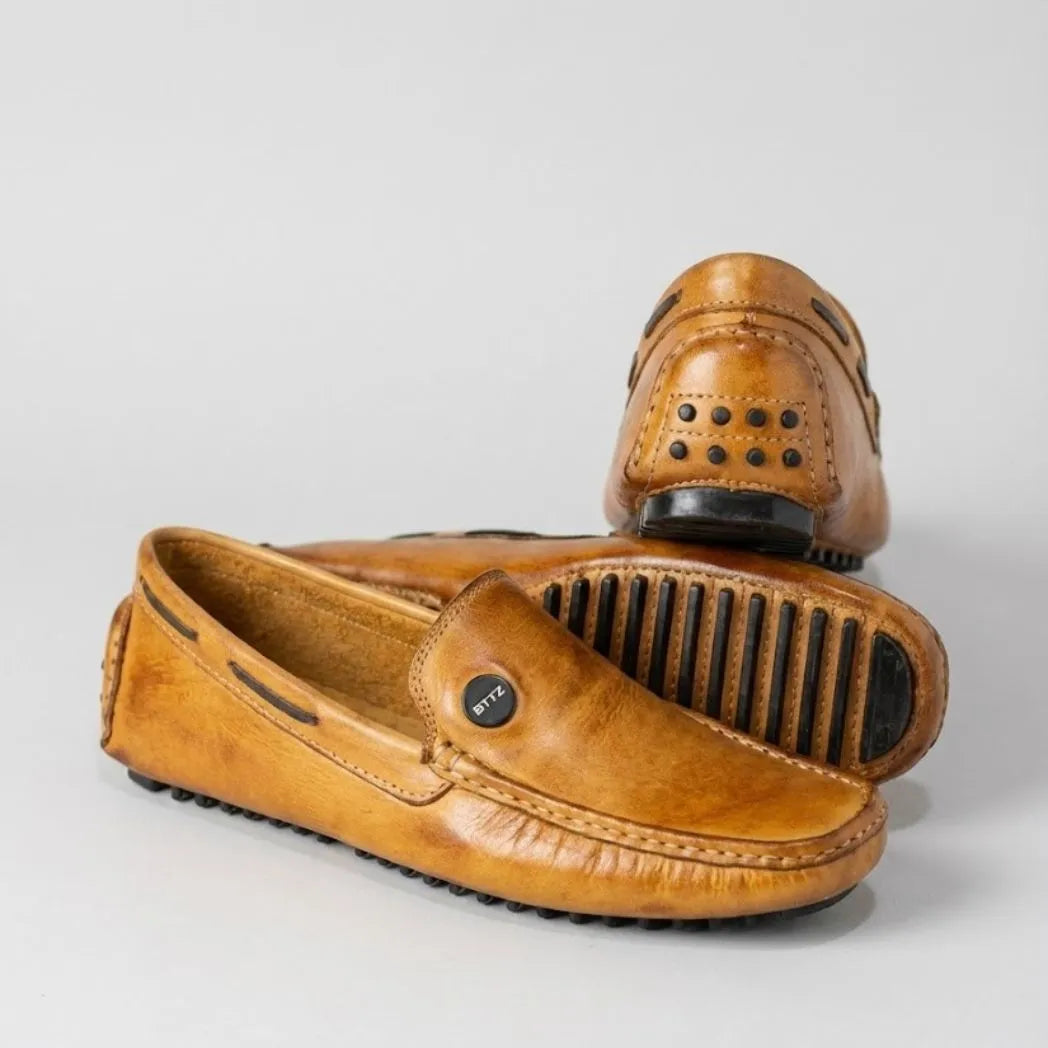Par do modelo Mocassim Driver Cruise de Couro Laranja, na cor laranja, com um dos solados voltado para a câmera.