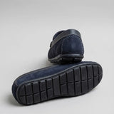 Par do modelo Mocassim Driver Dune de Camurça, na cor preto, com um dos solados voltado para a câmera.