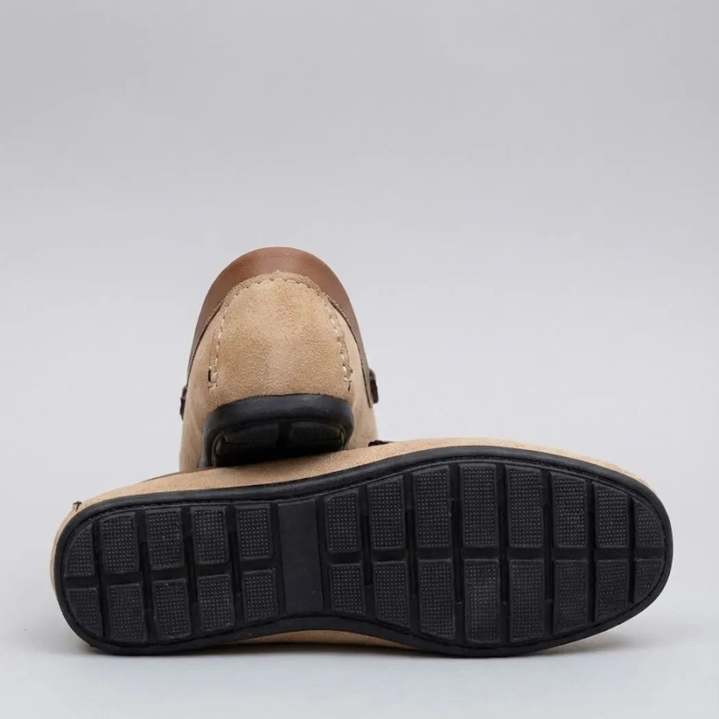 Par do modelo Mocassim Driver Dune de Camurça, na cor bege, com um dos solados voltado para a câmera.