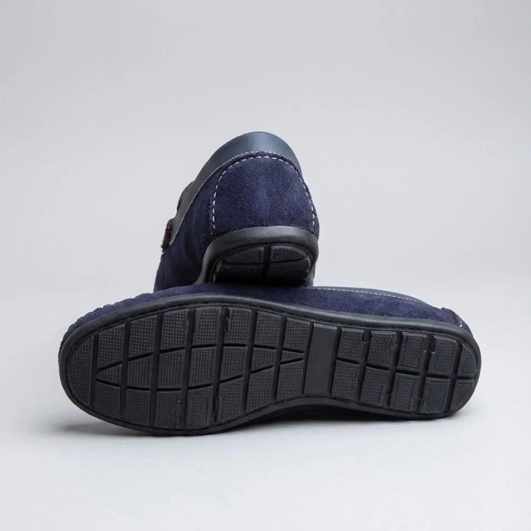 Par do modelo Mocassim Driver Dune de Camurça, na cor azul-escuro, com um dos solados voltado para a câmera.