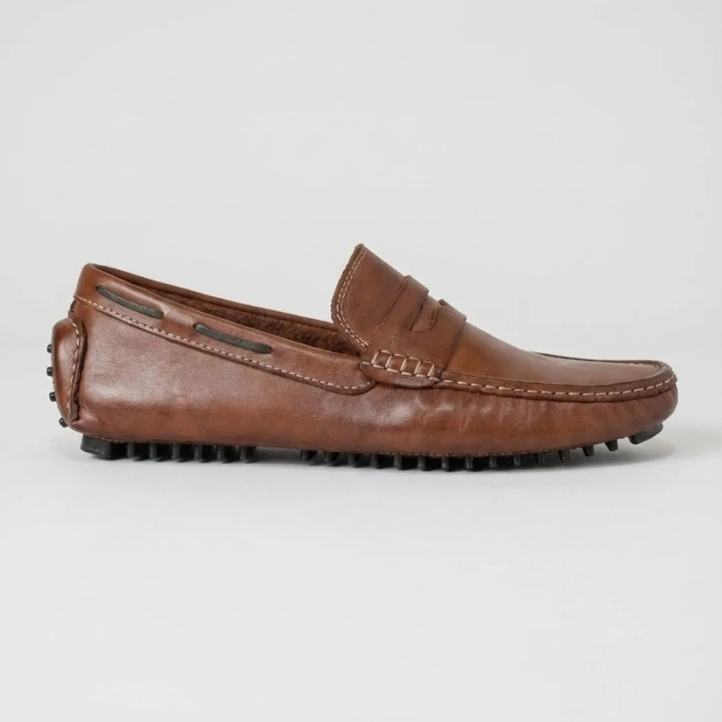 Mocassim Driver Penny de Couro: modelo marrom de perfil, com faixa frontal, cordão nas laterais e sola preta.