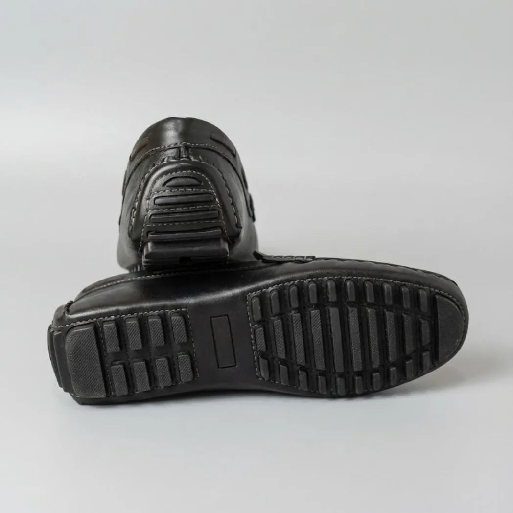 Par do modelo Mocassim Driver Penny de Couro, na cor preto, com um dos solados voltado para a câmera.