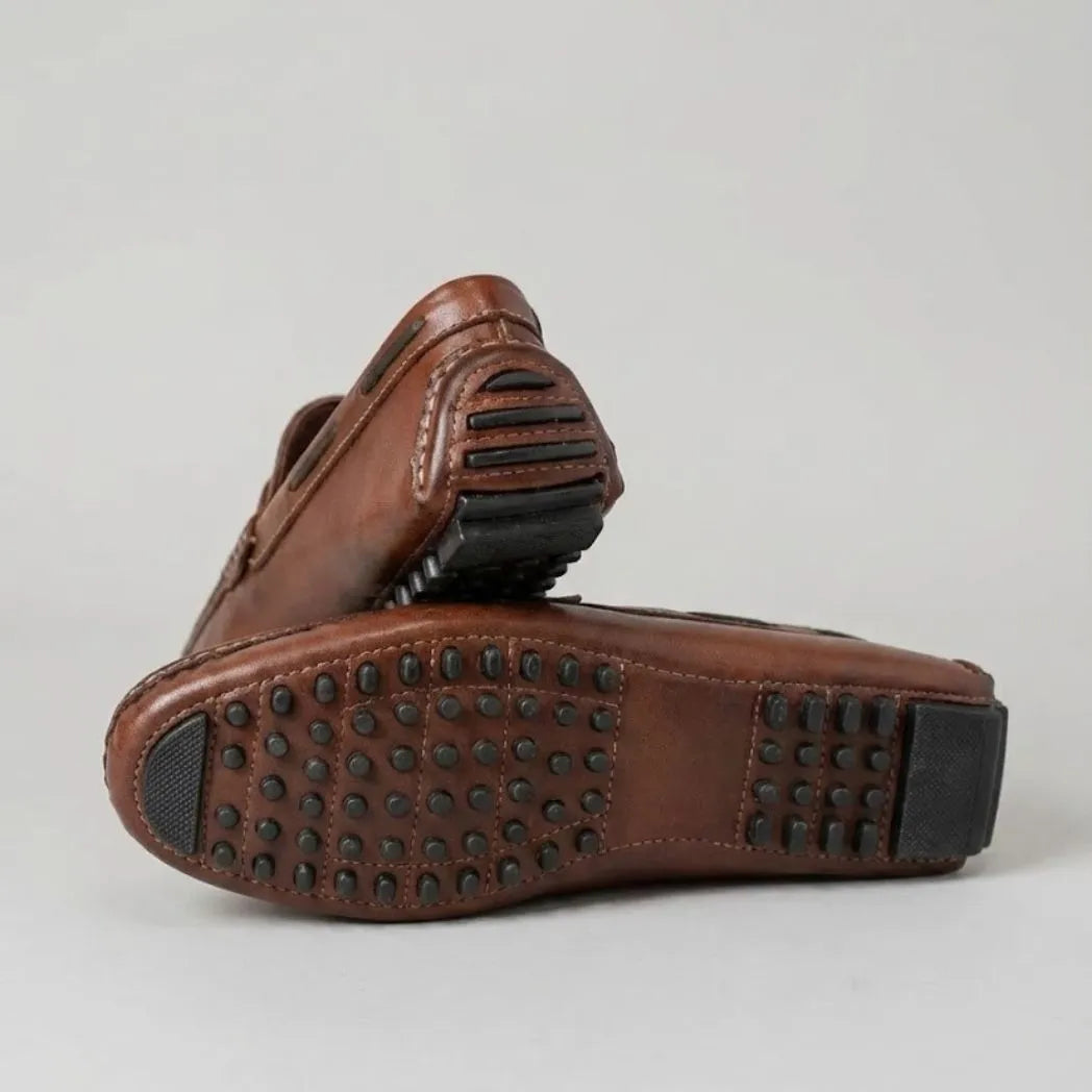 Par do modelo Mocassim Driver Penny de Couro, na cor marrom, com um dos solados voltado para a câmera.