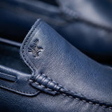 Mocassim Driver Vancouver de Couro Azul: detalhe do couro azul, costura e emblema em baixo relevo, sem metal acrescentado.