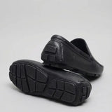 Par do modelo Mocassim Driver Vancouver de Couro, na cor preto, com um dos solados voltado para a câmera.