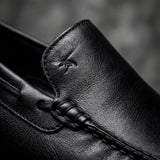 Mocassim Driver Vancouver de Couro Preto: detalhe da costura preta, couro e emblema em baixo relevo, sem ilhós dourado.