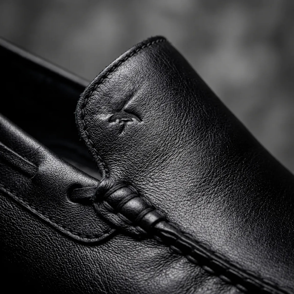 Mocassim Driver Vancouver de Couro Preto: detalhe da costura preta, couro e emblema em baixo relevo, sem ilhós dourado.