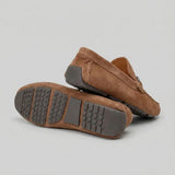 Par do modelo Mocassim Driver de Camurça Capri Dune, na cor marrom, com um dos solados voltado para a câmera.