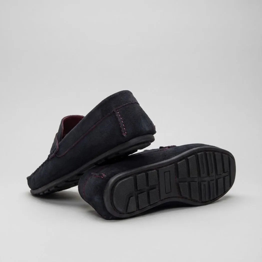 Par do modelo Mocassim Driver de Camurça Capri Tobacco, na cor escuro, com um dos solados voltado para a câmera.