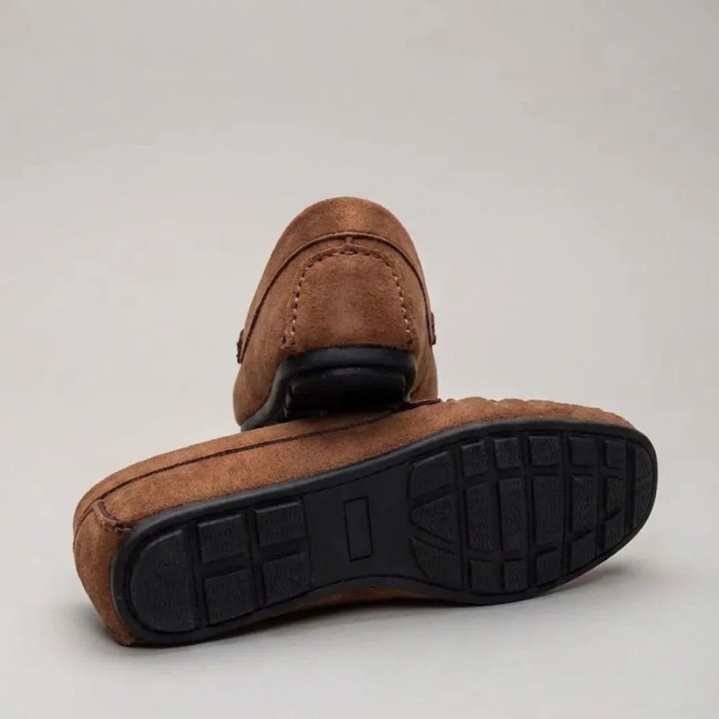 Par do modelo Mocassim Driver de Camurça Capri Tobacco, na cor marrom, com um dos solados voltado para a câmera.
