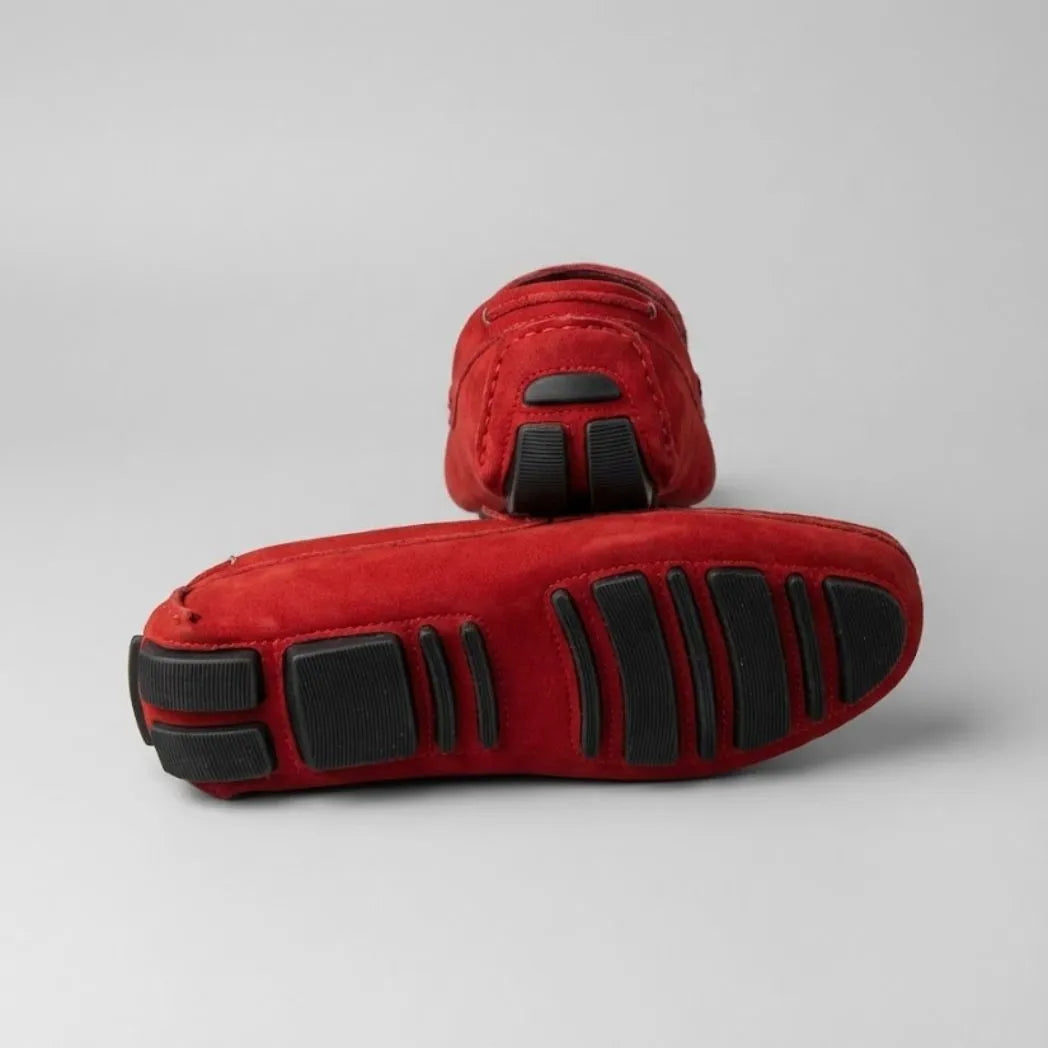 Par do modelo Mocassim Driver de Couro Capri Nero, na cor vermelho, com um dos solados voltado para a câmera.