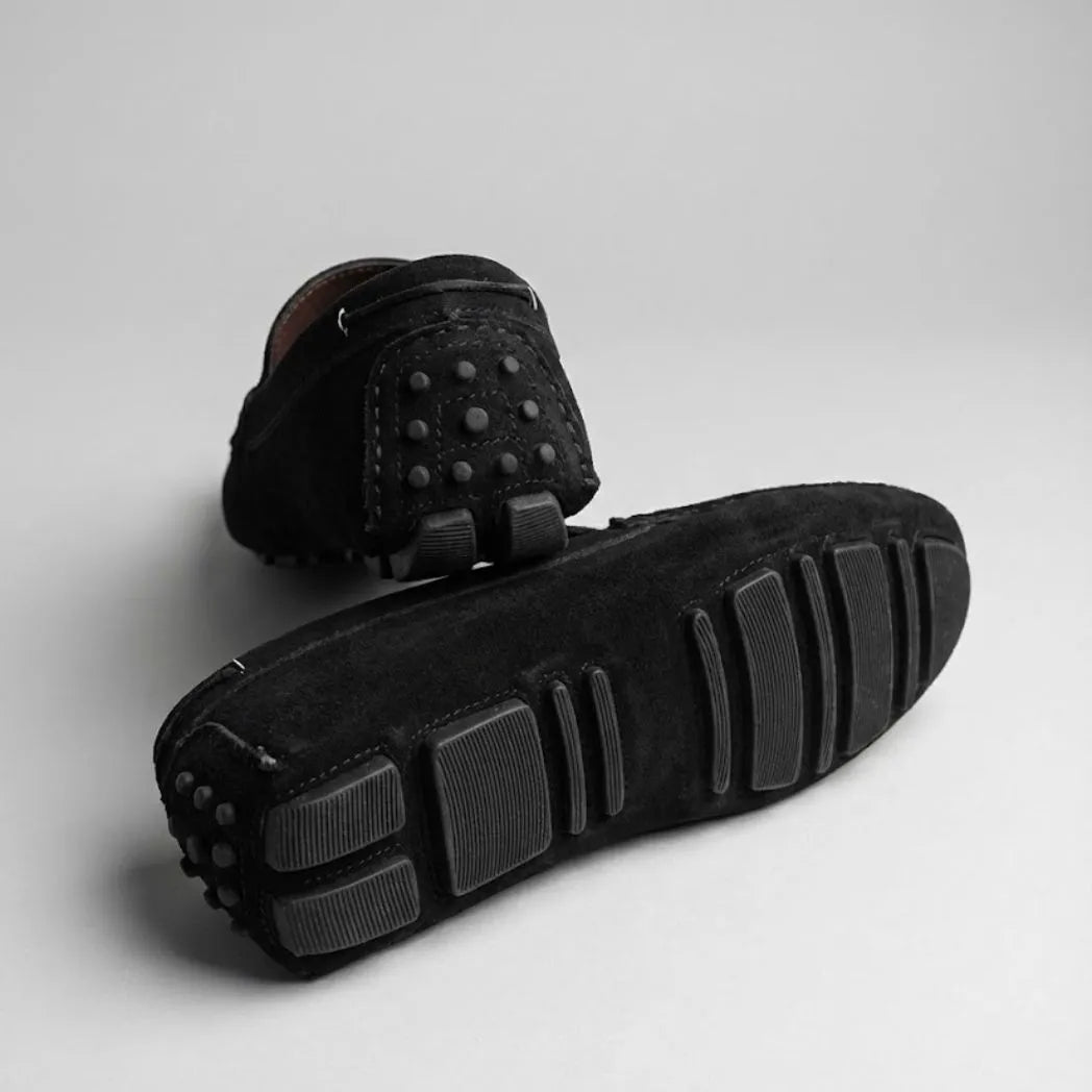 Par do modelo Mocassim Driver de Couro Capri Nero, na cor preto, com um dos solados voltado para a câmera.