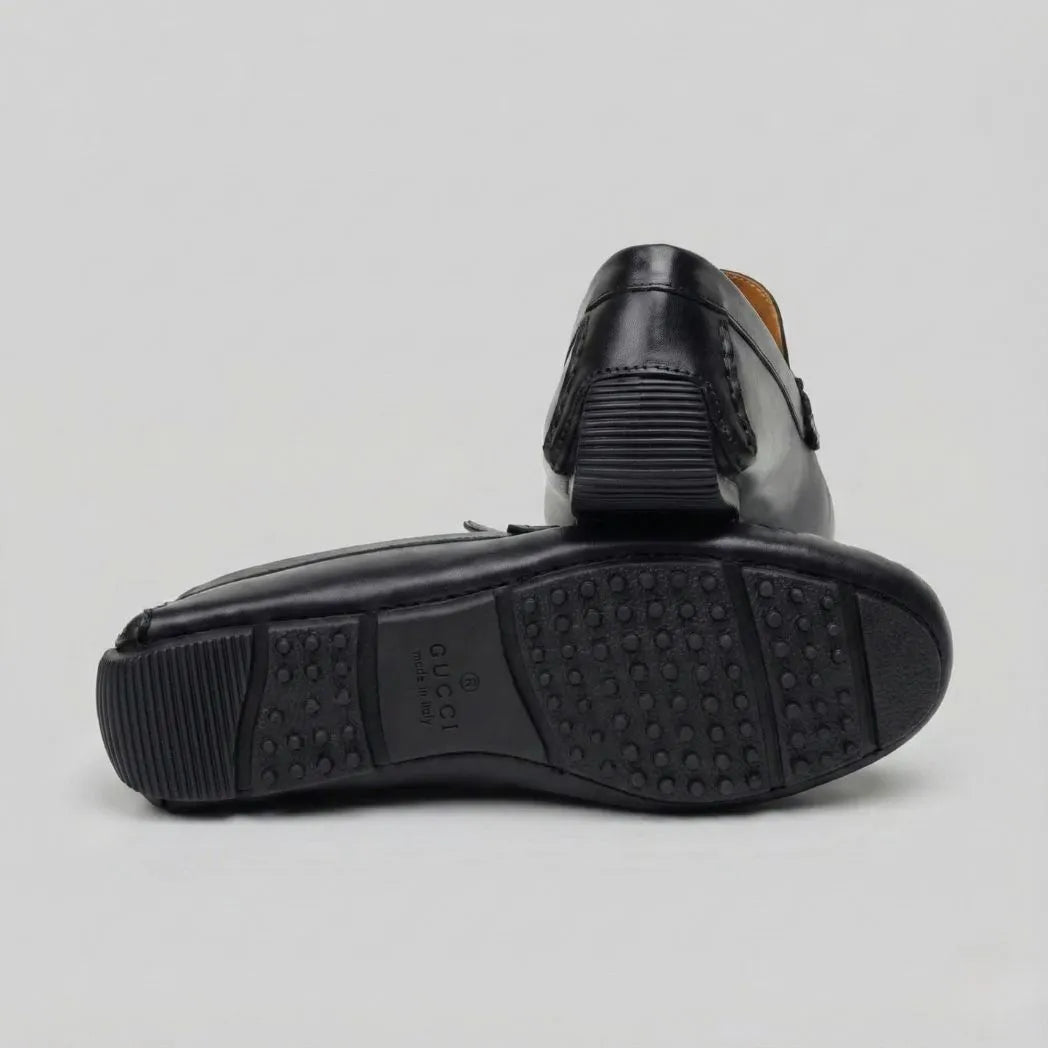 Par do modelo Mocassim Driver de Couro Portofino, na cor preto, com um dos solados voltado para a câmera.