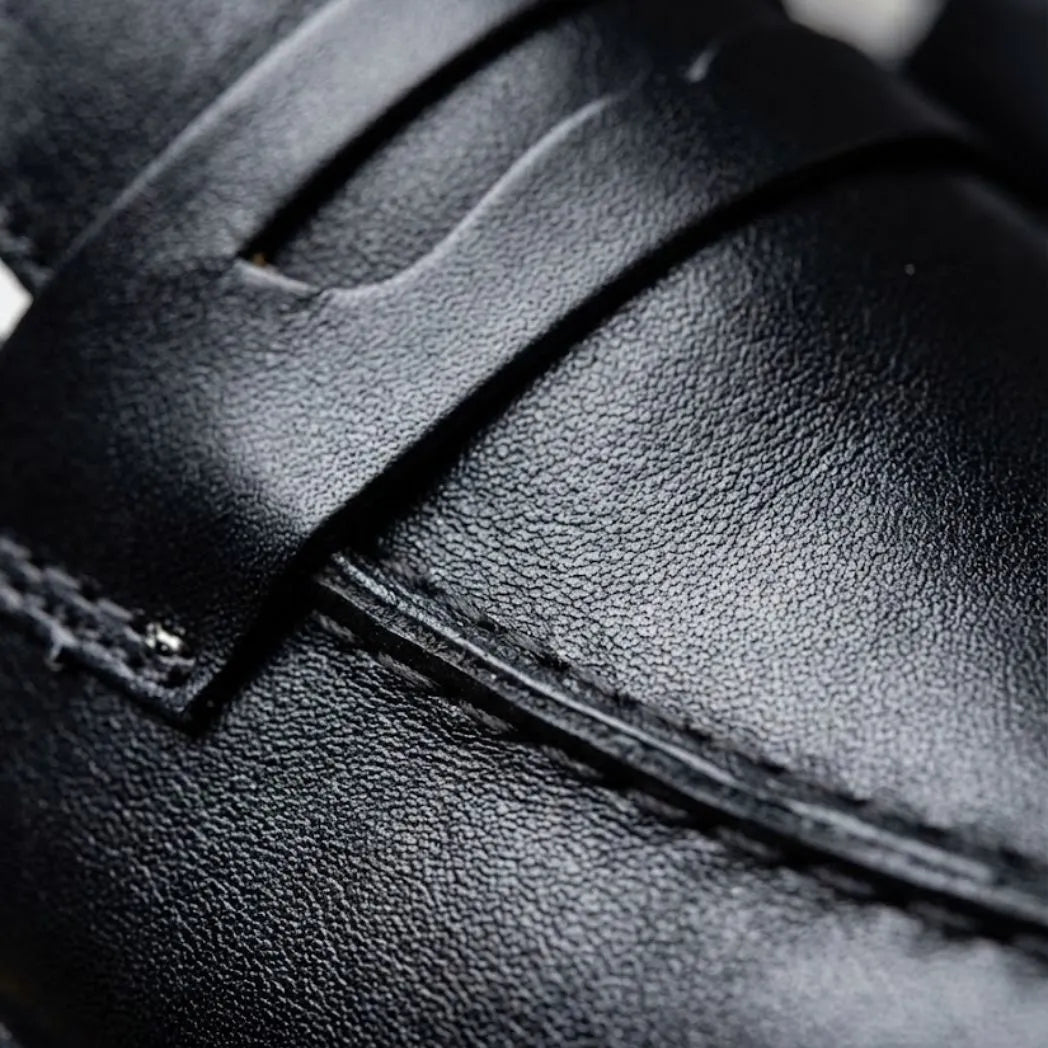 Mocassim Loafer Londres de Couro: detalhe da superfície preta, da faixa frontal e da costura.