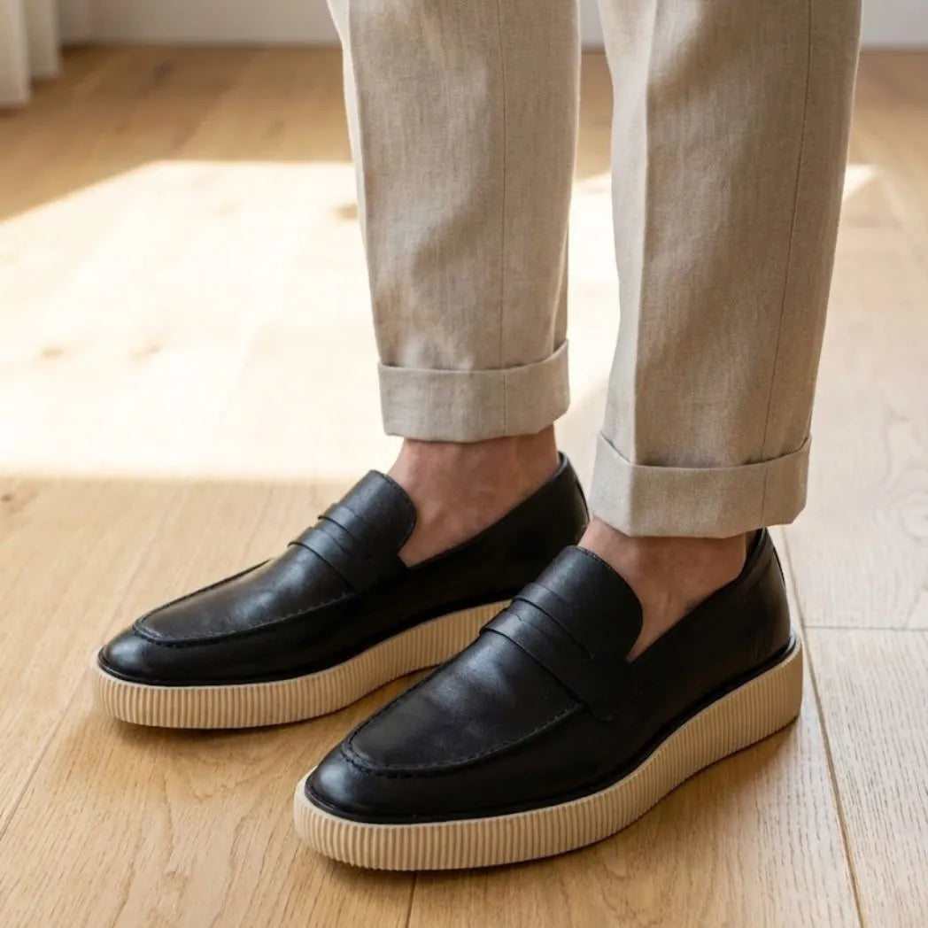 Mocassim Loafer Londres de Couro: par preto com sola bege usado com calça clara dobrada na barra.