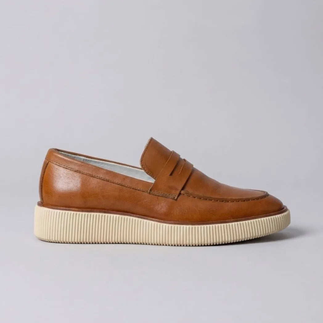 Mocassim Loafer Londres de Couro: modelo marrom de perfil, com faixa frontal e sola bege de borda estriada.