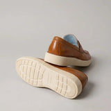 Mocassim Loafer Londres de Couro: par marrom com um sapato virado, mostrando a sola bege com sulcos.